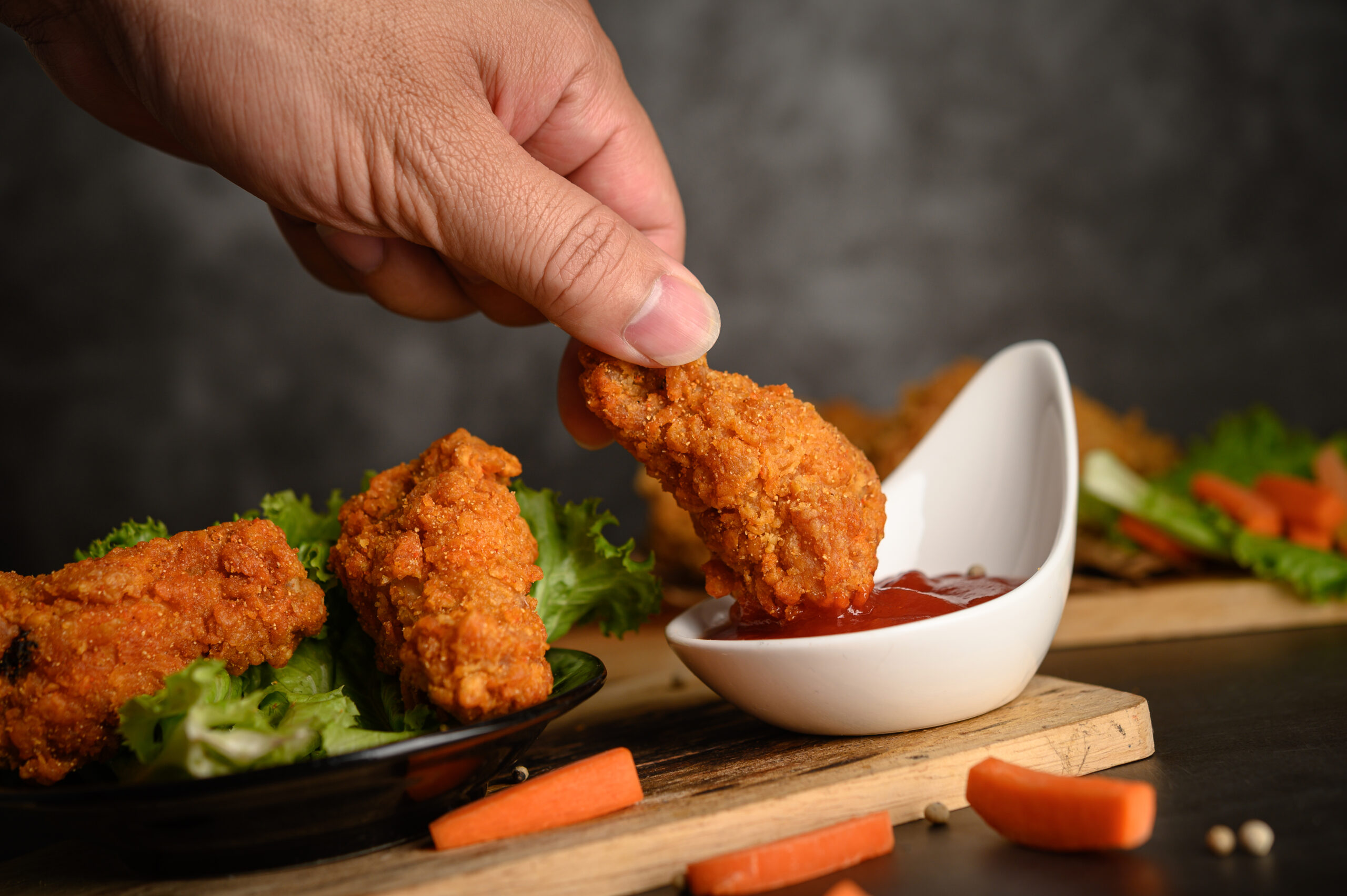 Hand holding crispy fried chicken dipped in tomato sauce. Selective focus.
