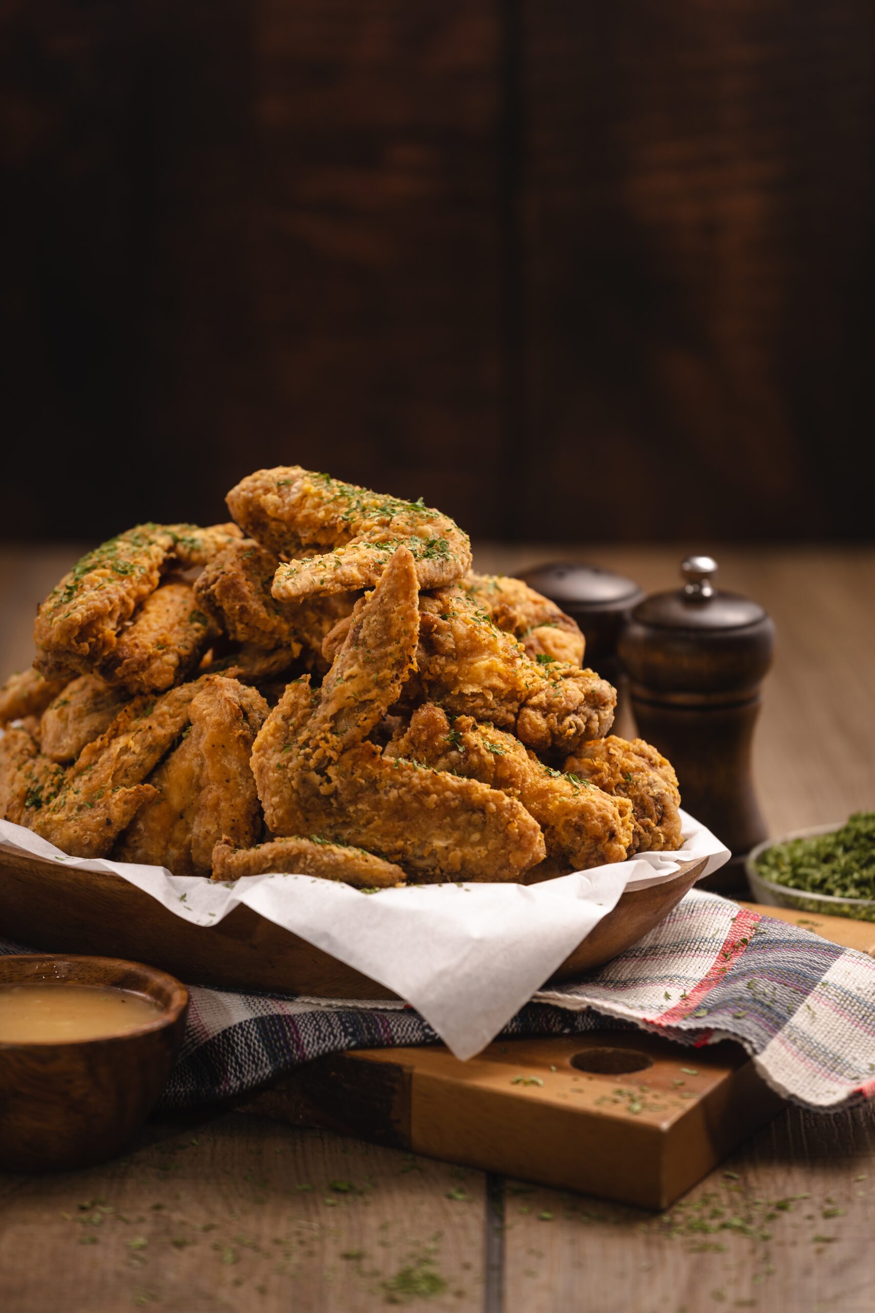 A vertical shot of a pile of fried chicken wings and some spices on a wooden table